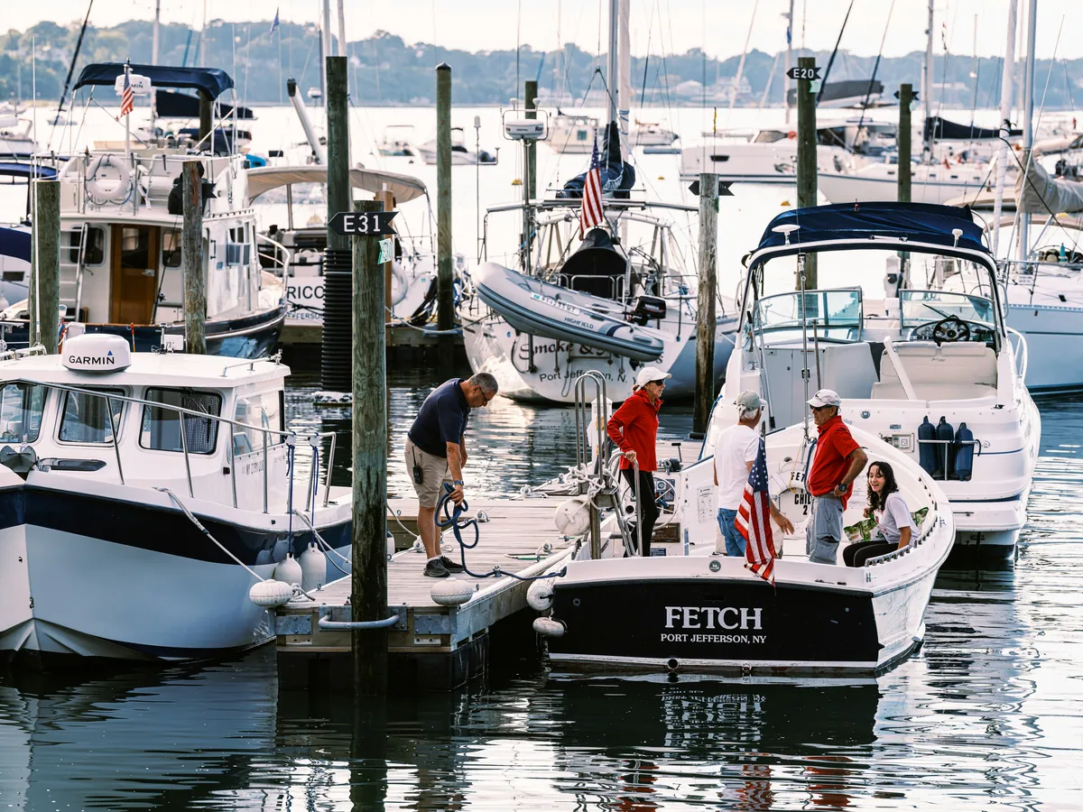 A dockhand helping a family board their motorboat in a busy marina