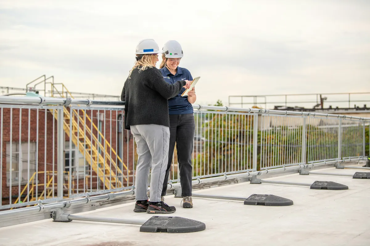 Two inspectors in hard hats reviewing a tablet on a flat rooftop